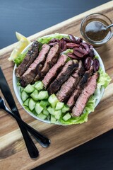 Vertical top view shot of the steak salad on a white plate with a sauce on a wooden board