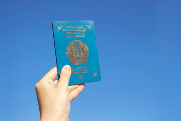 Hand holds the national passport of the Republic of Kazakhstan against the blue sky background. High quality photo.