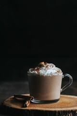 Vertical closeup shot of a glass of hot chocolate on a wooden board, with cream on top