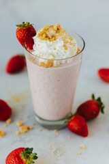Vertical closeup shot of a glass of a strawberry milkshake surrounded by strawberries
