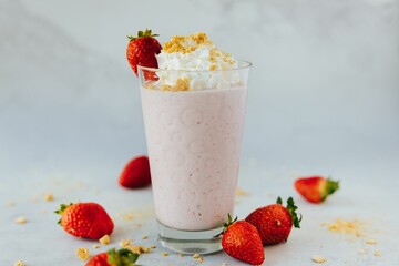 Closeup shot of a glass of a strawberry milkshake surrounded by strawberries with cream on top