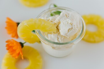 Top view of a glass of ice cream surrounded by sliced pineapples and an orange flower