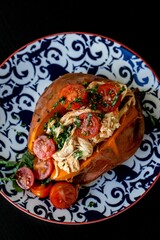 Top view of a baked sweat potato loaded with cherry tomatoes, meat and greens