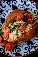 Top view of a baked sweat potato loaded with cherry tomatoes, meat and greens