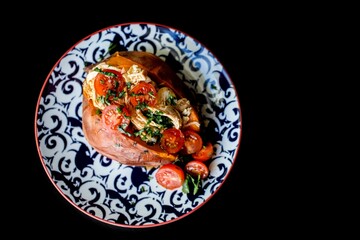 Top view of a baked sweat potato loaded with cherry tomatoes, meat and greens