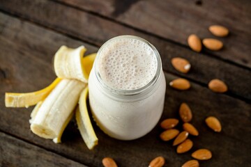 Top view shot of a banana protein shake with a half banana and almond nuts on the table