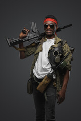 Studio shot of military man of african ethnic with red headband and rifle.