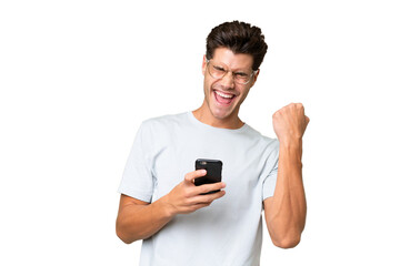Fototapeta na wymiar Young caucasian handsome man over isolated background with phone in victory position