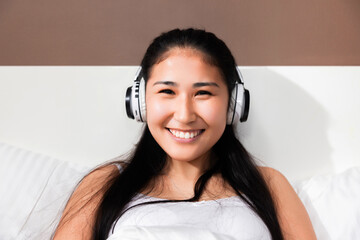 Portrait of cheerful pretty young asian korean student girl in modern new last serie headphones earphones smiling while listening to music relaxing in the early morning.