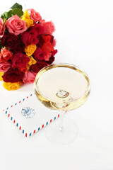 A letter in an envelope with a glass of champagne on a white background. Bouquet of roses is out of focus. Concept of the holiday.Flat lay. Top view. Copy space.Isolated object. Vertical photo.I