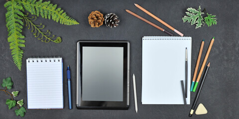  Sketchbook with white sheets, digital tablet mockup ,  notebook, pen ,eraser, pastel pencils, decorative green plants on the black   background. Top view. Business, art lessons, education concept