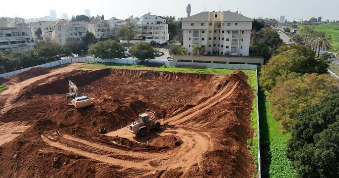 Aerial footage of Wheel Loader and a bagger working on a hill at a construction site and preparing the area for construction work. Filmed in C4K Apple ProRes 422 HQ