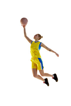 Full-length image of young sportive girl, basketball player in motion, jumping with ball against white studio background. Concept of professional sport, hobby, healthy lifestyle, action and motion