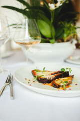 Grilled vegetables in a large white plate. A glass of rose wine on a light background.