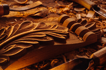 Art wood carving. Carved wooden big leaf on wooden background with shaving. Chisels on background.
