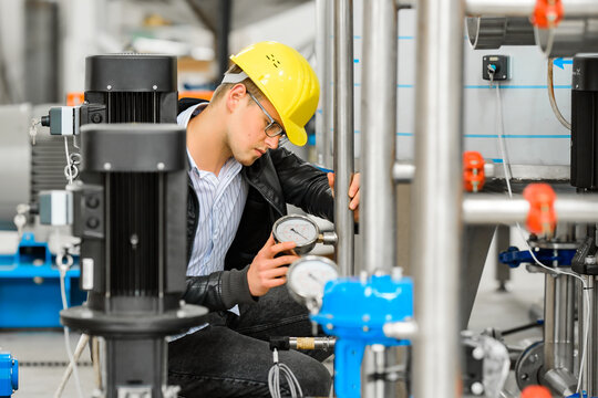 A young engineer works at a chemical factory, inspecting pressure gauge readings. Chemical industry equipment.