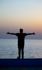 Man looking out to sea with open arms at sunset. Feeling free and alive in the embrace of the sea at dusk.