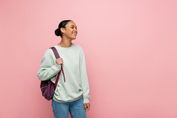 Cheerful african american student with backpack looking away isolated on pink.