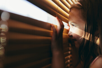 Young girl looking through blinds - obrazy, fototapety, plakaty