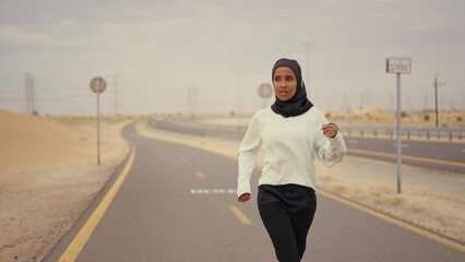 Beautiful female runner wearing sport abaya running in the desert in dubai, united arab emirates. Concept about sport, and muslim culture