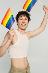 carefree bigender person in crop top standing with small lgbt flags isolated on grey.