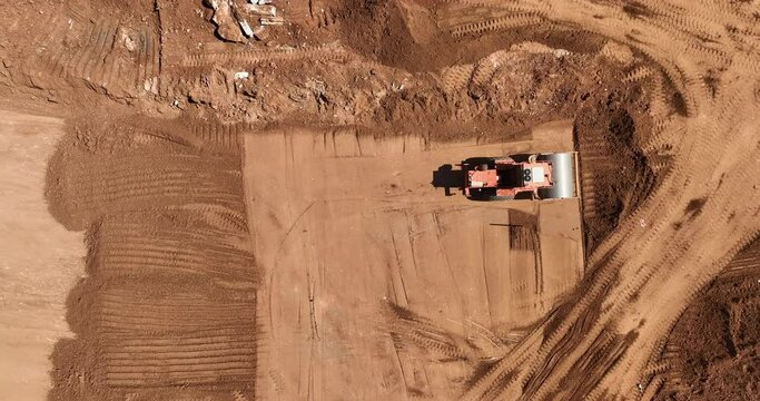 Aerial footage of a loader and a vibratory soil compactor working on a construction site and preparing the area for construction work. Filmed in C4K Apple ProRes 422 HQ