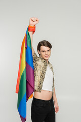 happy bigender person with lgbt flag showing win gesture and smiling at camera isolated on grey.