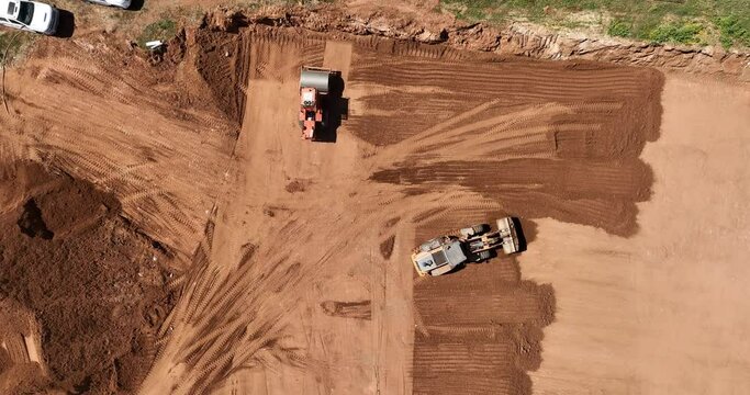 Aerial footage of a loader and a vibratory soil compactor working on a construction site and preparing the area for construction work. Filmed in C4K Apple ProRes 422 HQ