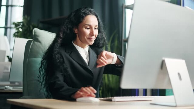 Happy smiling multiethnic businesswoman looking at watch counting waiting for the seconds until the end of the working day and leaves the workplace elated Pretty office worker excited before weekend