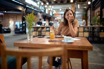 Young woman at coffee shop. Girl in casual clothes enjoying her cup of coffee, smiling.