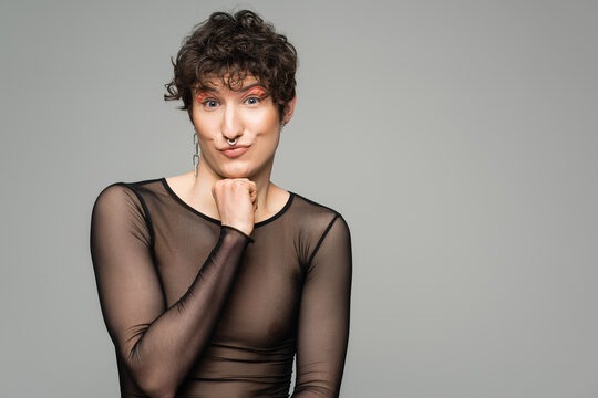 smiling bigender model in black transparent top and silver accessories looking at camera isolated on grey.