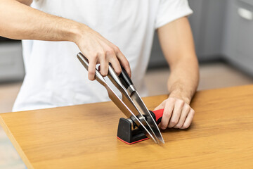 Close-up photo of man sharpening knives with special knife sharpener at home