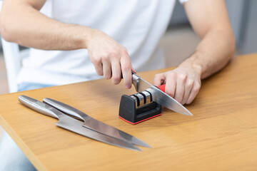 Close-up photo of man sharpening knives with special knife sharpener at home - obrazy, fototapety, plakaty