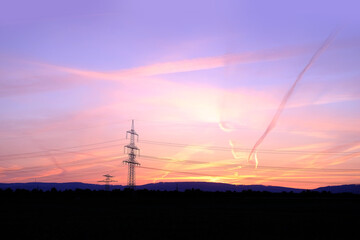 beautiful landscape, sky with airplane trail lines, power towers, field in evening in rays of...