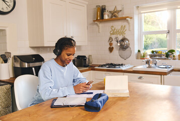 Teen girl doing homework and using phone texting smiling