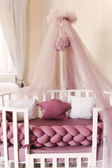 Baby pink four-poster bed with pompoms and pillows