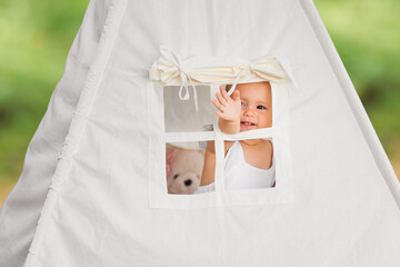 Little happy baby girl in toy canvas house wigwam outdoors. © Olha