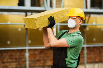 Builder holds mat of mineral wool for insulating buildings. Worker insulating house facade with mineral rock wool.