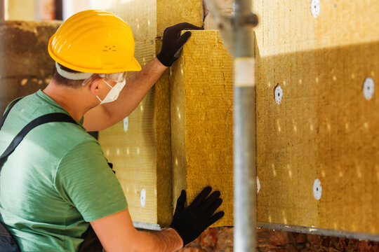 Construction worker insulates brick wall of house with mats of rock wool. Modern insulating materials for warming buildings.
