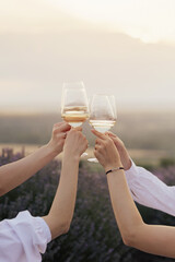 Group of friends with white wine in hands clinking with glasses. Close-up of hands and drinks.