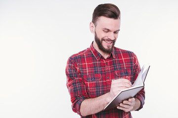 Portrait with copy space of thoughtful, serious, bearded man holding copybook and pen with success expression over white background. Study and teaching