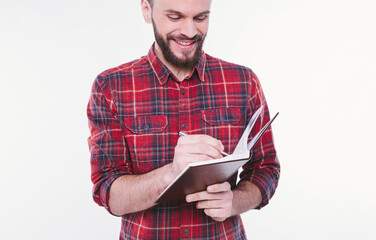 Portrait with copy space of thoughtful, serious, bearded man holding copybook and pen with success expression over white background. Study and teaching