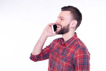 Young smiling happy cheerful bearded man in plaid shirt talks on mobile or cell phone, conducting...