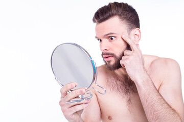 Close up portrait of frustrated, naked bearded man looking in the mirror for acne on his face isolated on white background