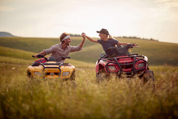 Two excited friends driving quad together; Active vacation concept