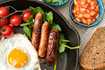 Traditional english breakfast with eggs, beans and sausages on a cast iron pan