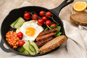 Traditional english breakfast with eggs, beans and sausages on a cast iron pan