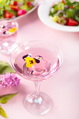 Glass of pink violet purple cocktail decorated flowers viola pancies