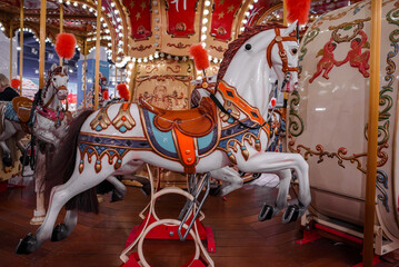 Fototapeta na wymiar Old French carousel in a holiday park. Three horses and airplane on a traditional fairground vintage carousel. Merry-go-round with horses.