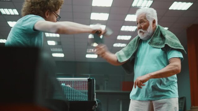 Elderly table tennis coach teaches teenager forehand and backhand exercises in ping pong